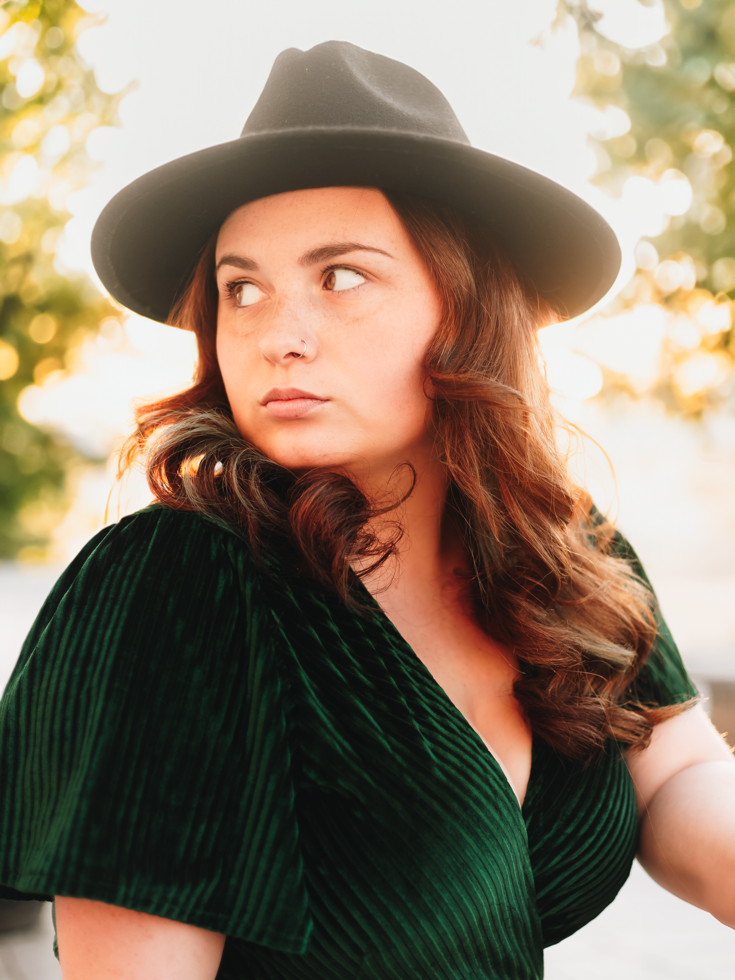 Portrait series in emerald velvet dress and wide-brimmed hat against golden sunset light.
