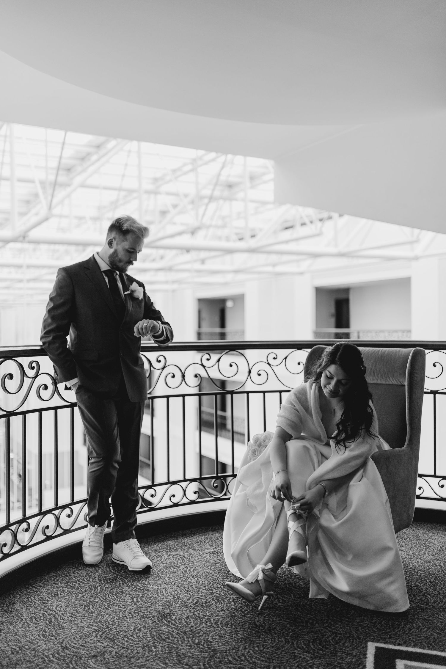 Black and white wedding moment on balcony with couple adjusting attire.
