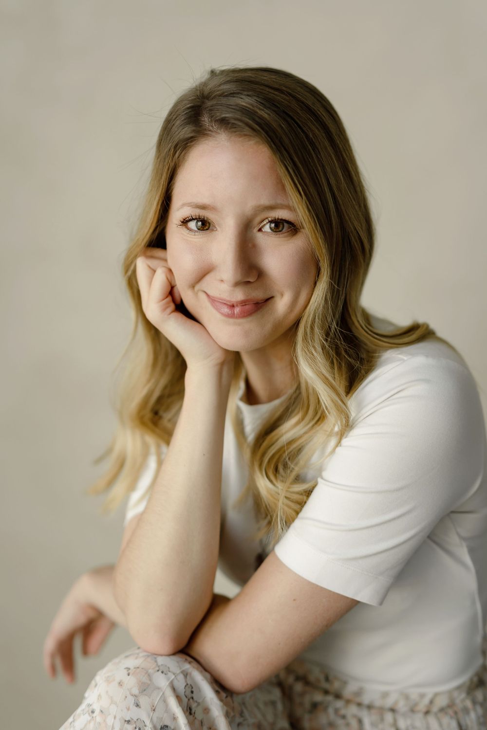 Natural light portrait showing casual pose and gentle smile against neutral background.
