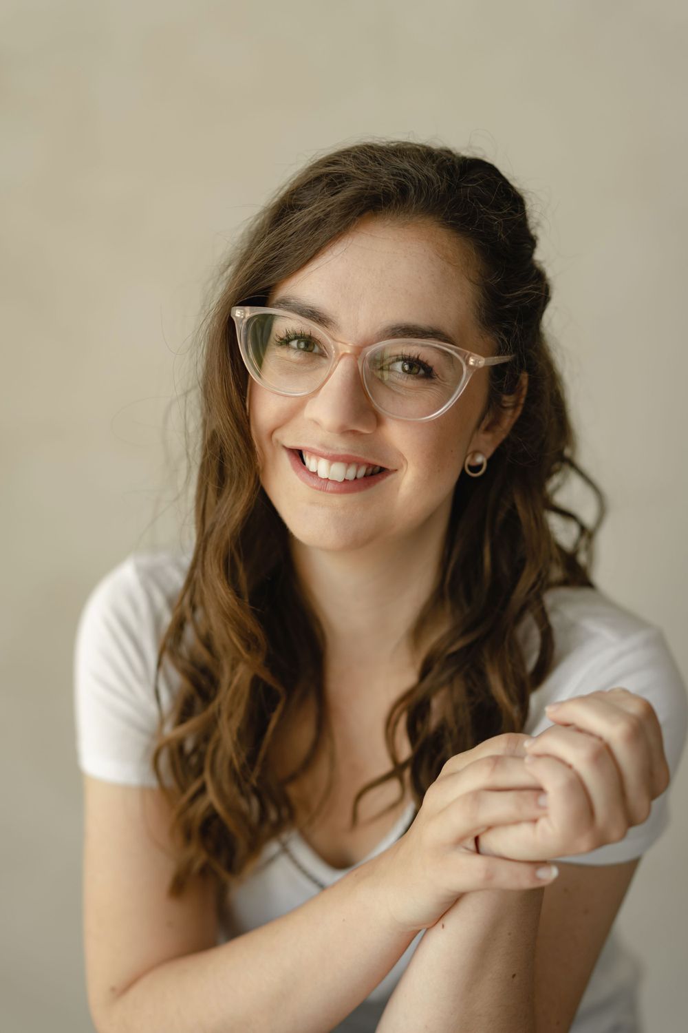 Cheerful portrait showing glasses and curly hair against light background.
