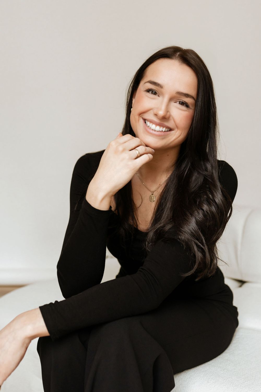 Studio portrait of person in black sweater with long dark hair and bright smile.