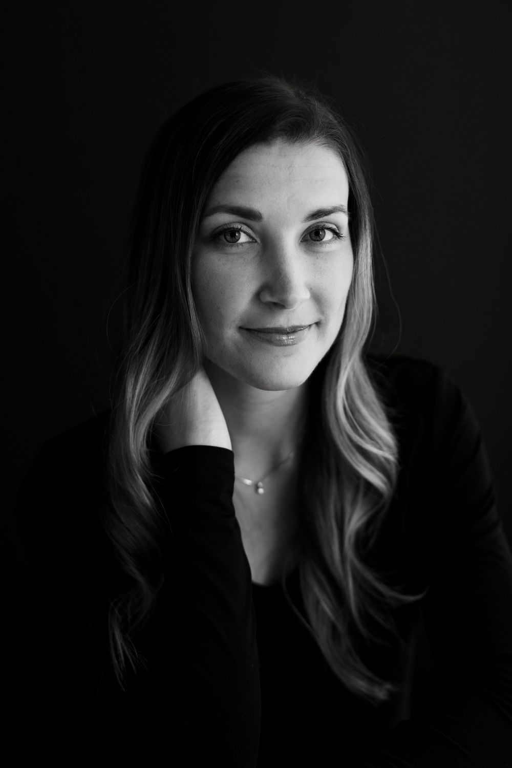Dramatic black and white headshot with soft lighting and subtle smile.