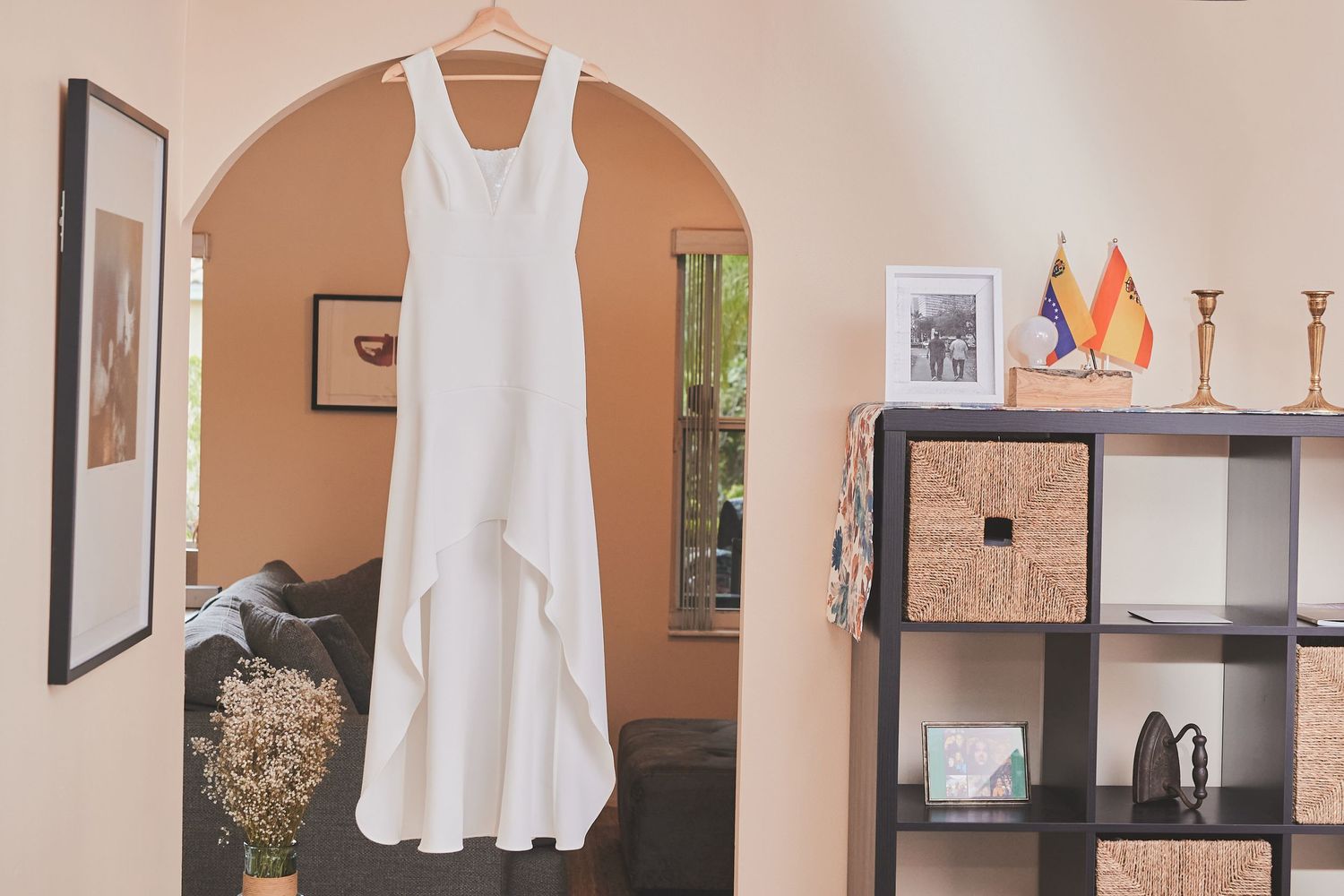 White wedding dress hanging on display in archway with home decor visible in background.