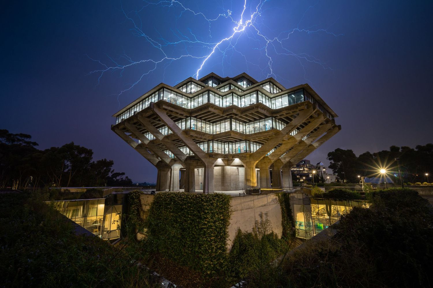 Modern brutalist architecture with honeycomb roof illuminated at night as lightning strikes in the background.