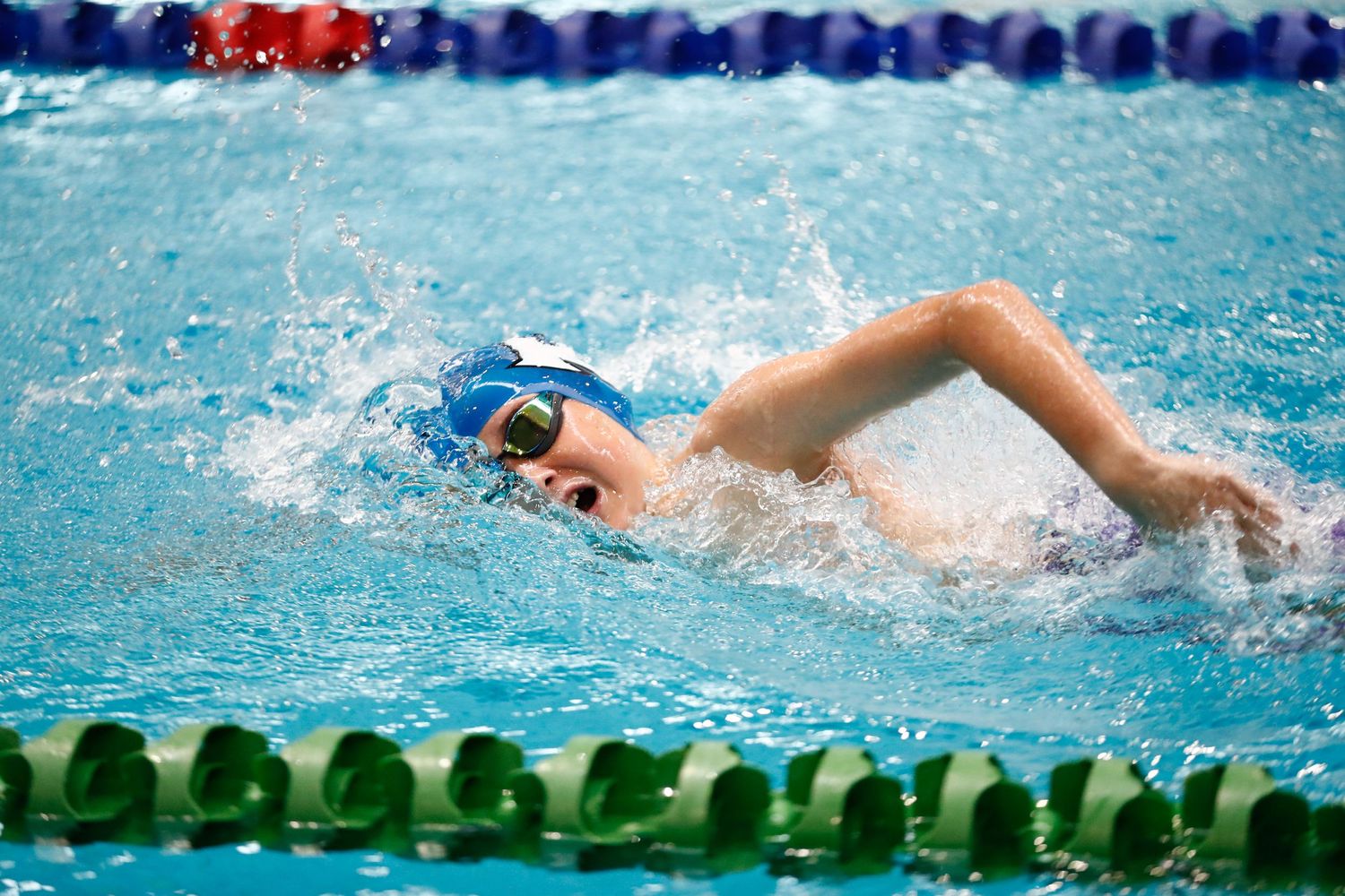 Competitive swimmer performing freestyle stroke in blue pool water with lane dividers.