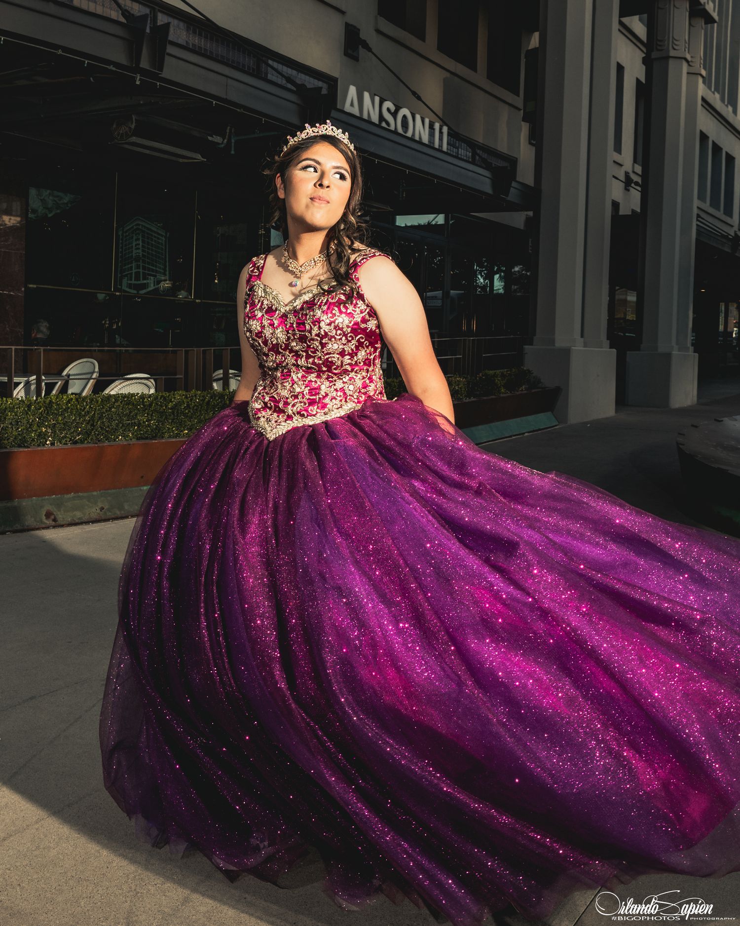 A quinceañera portrait featuring a sparkling purple ball gown outside an urban storefront.