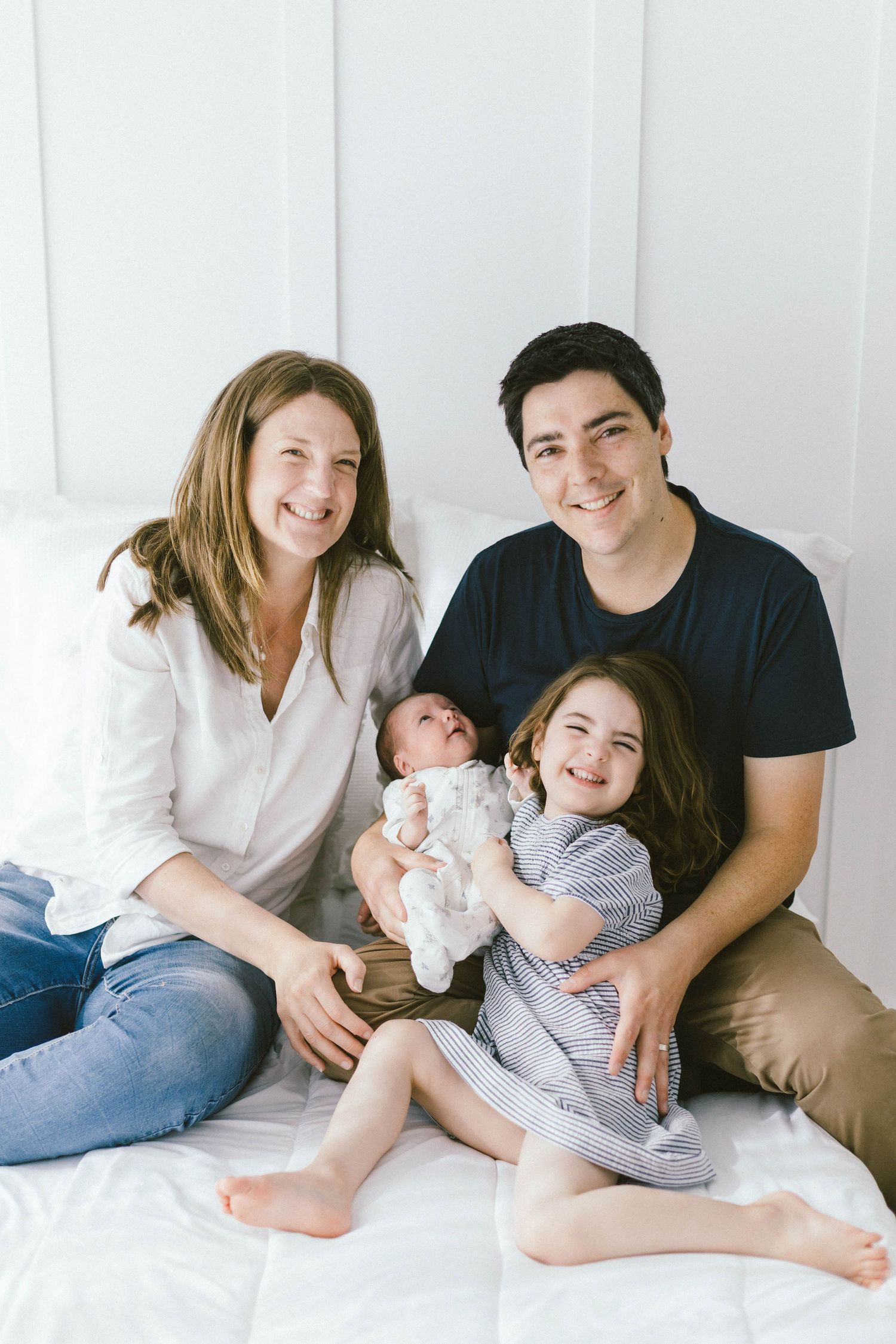 Family portrait with newborn baby against white wall.