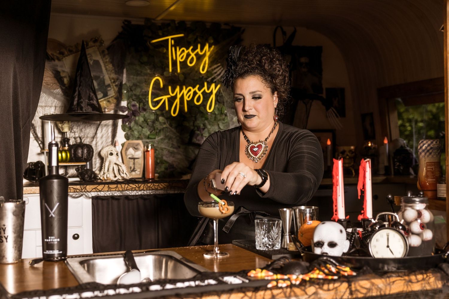 Bartender crafting cocktails at a spooky Halloween-themed bar with decorative props.