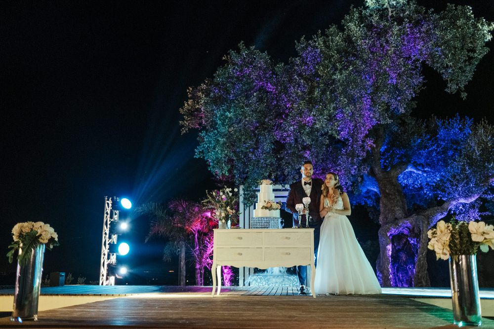 Cerimónia de casamento preparada debaixo de árvores com iluminação azul e roxa, criando um ambiente encantador.