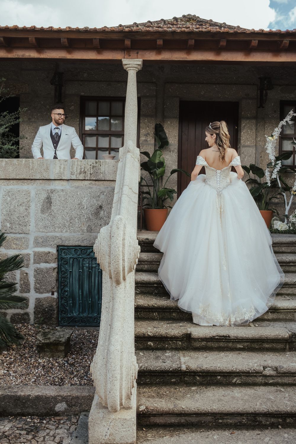 Um belo vestido de noiva em destaque contra uma arquitetura rústica de pedra e colunas.