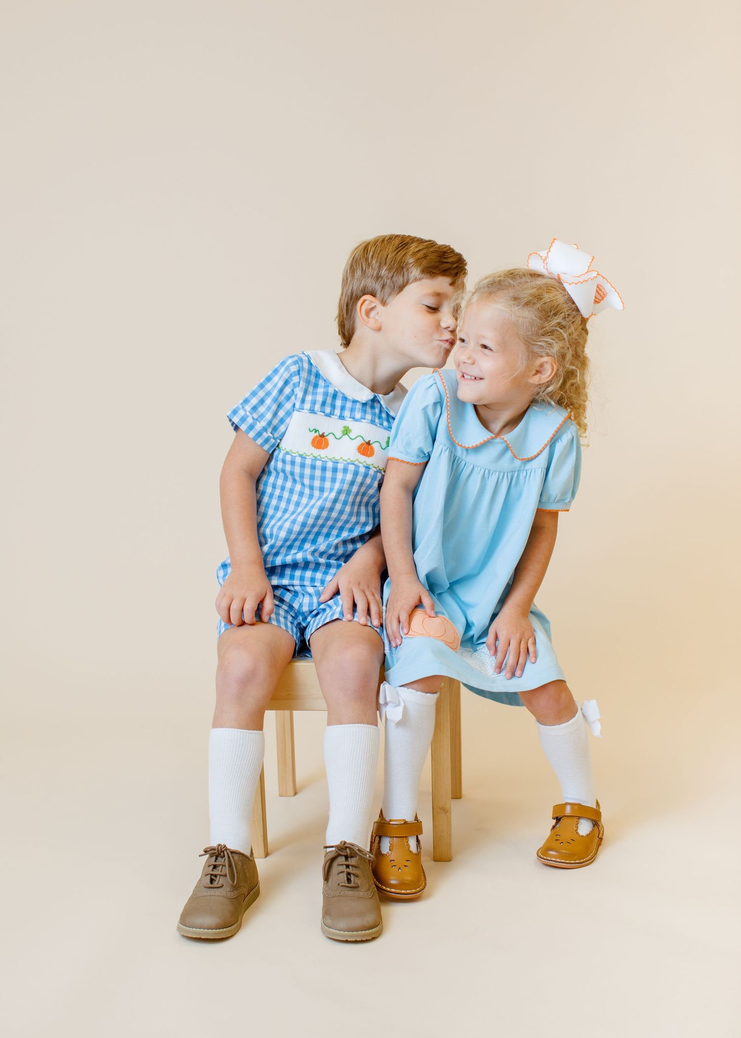 Two children in coordinating blue outfits sitting close together on wooden chair.