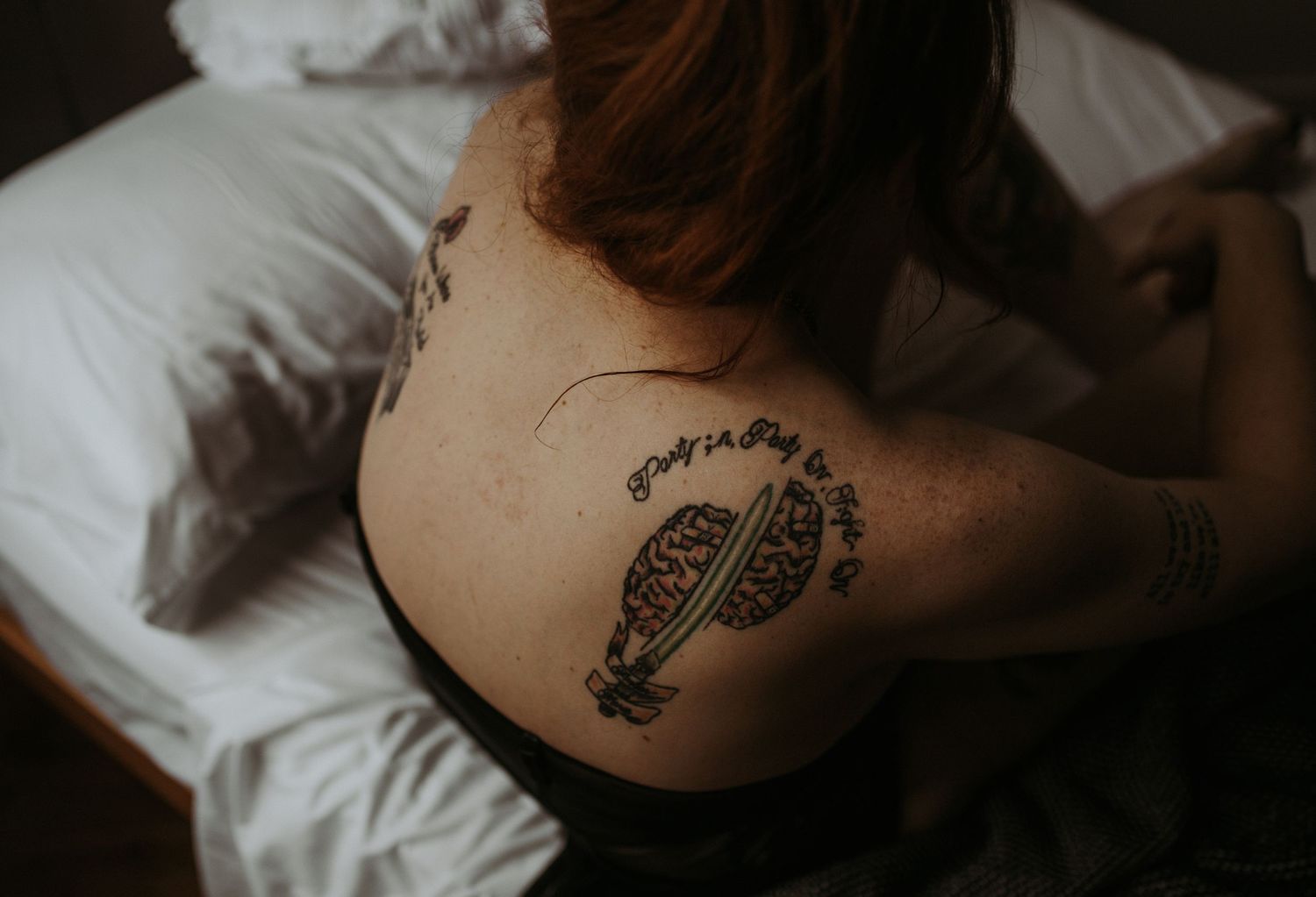 A detailed photograph of a back tattoo visible on someone's shoulder blade while sitting on top of white bedding.