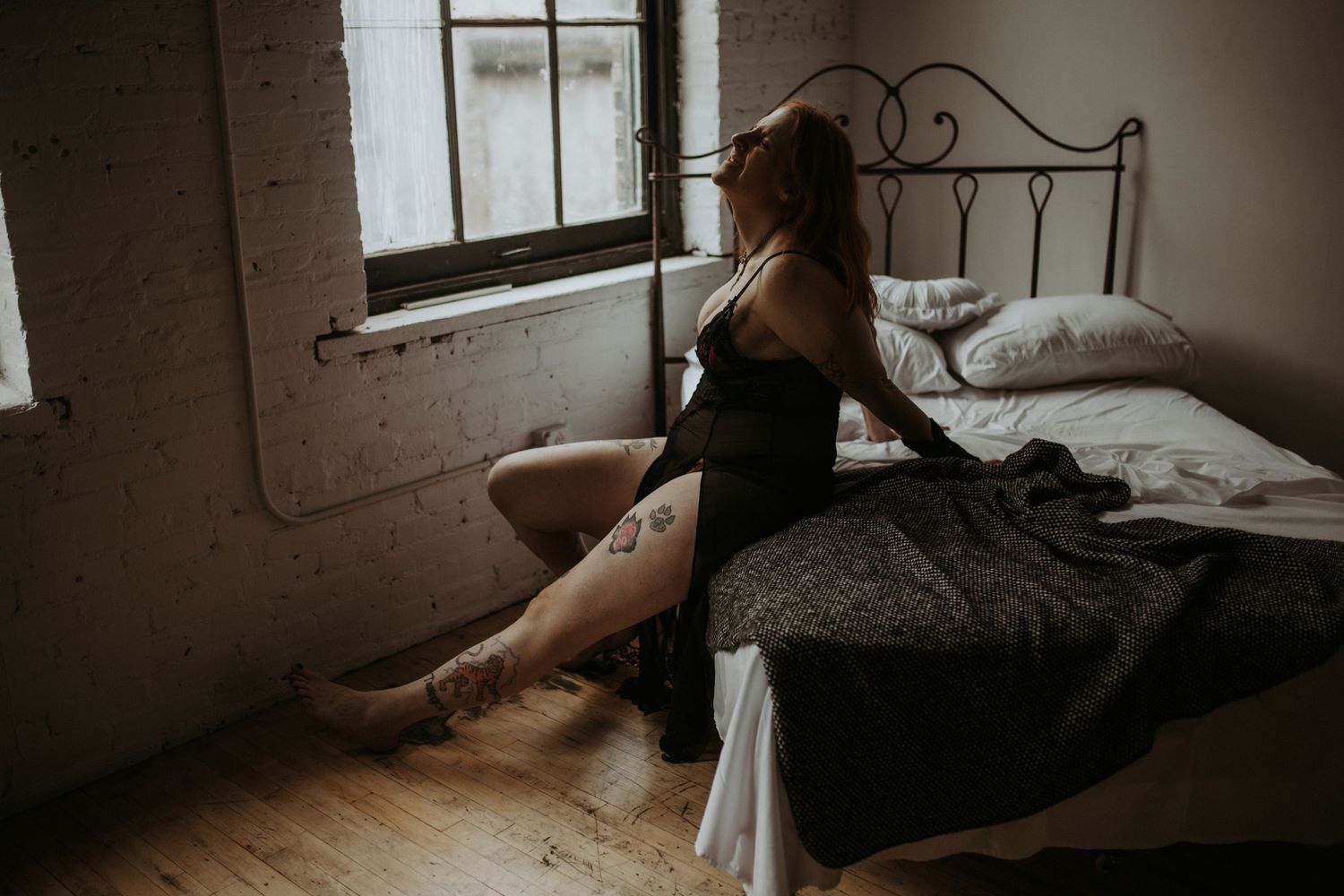 A silhouette lounges on an unmade bed looking out a sunny window in a moody, atmospheric bedroom scene.