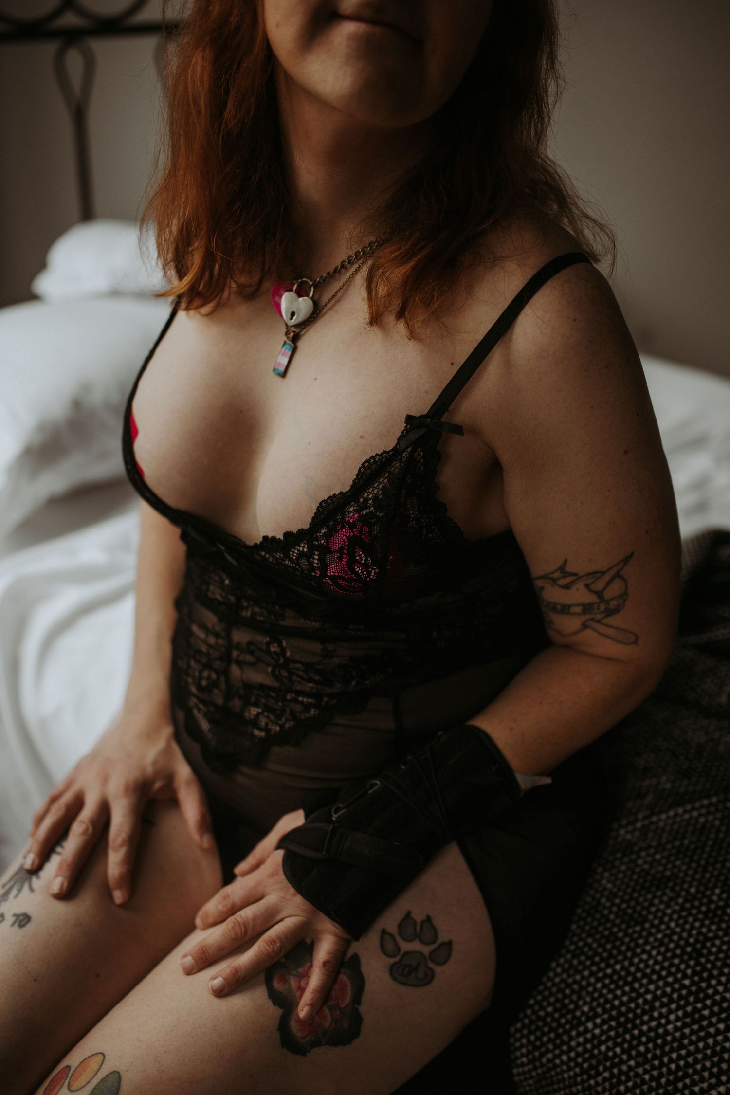 Moody boudoir photo showing lingerie, tattoos and jewelry details in dark atmospheric lighting.