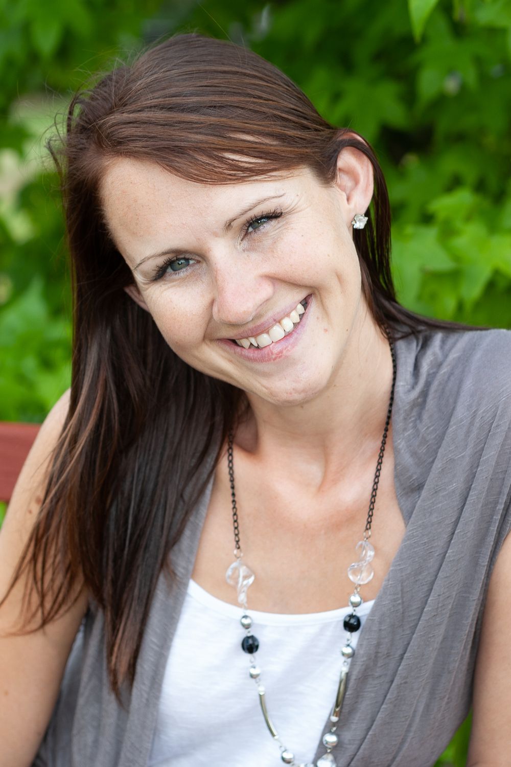 Outdoor portrait featuring casual style with beaded necklace against green foliage.