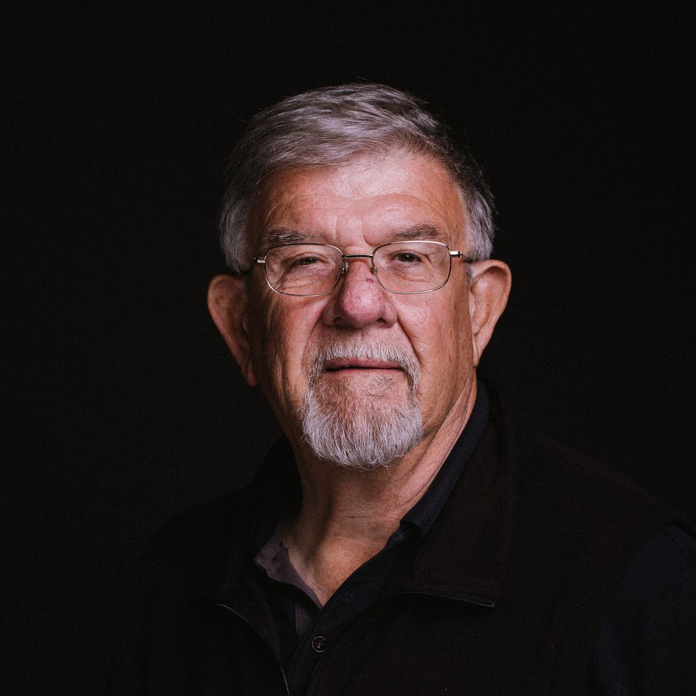 Dramatic portrait of senior person wearing glasses against black background.