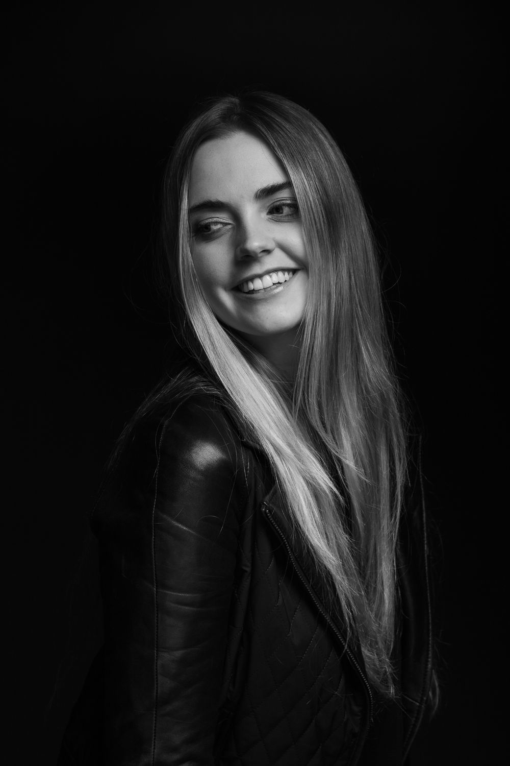 Black and white portrait showcasing long hair and joyful expression against dark backdrop.