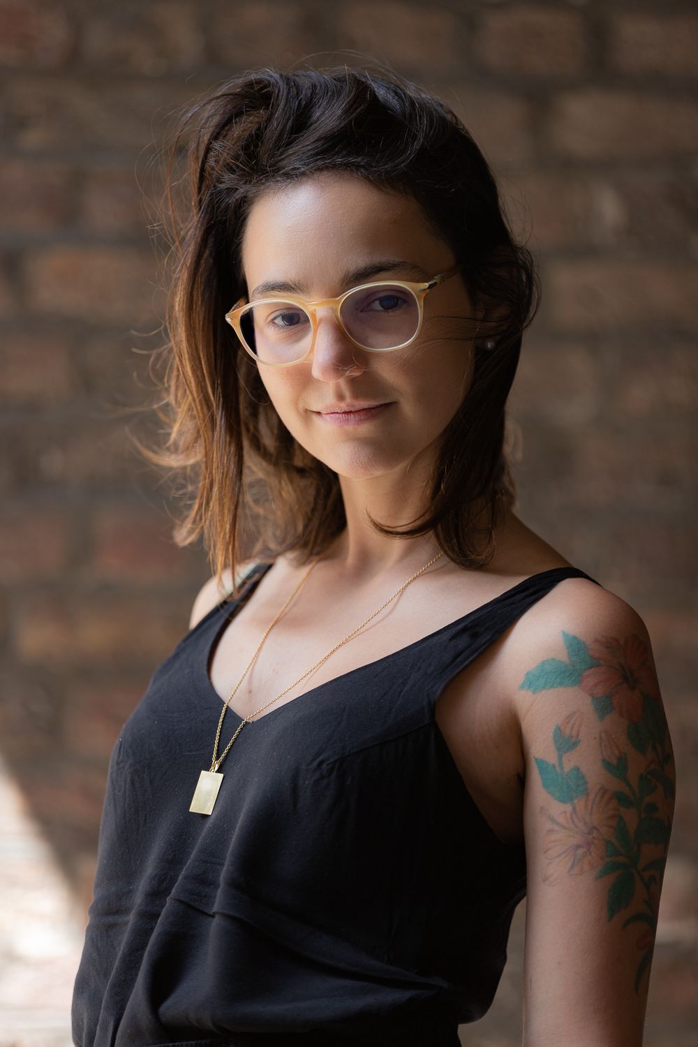 Portrait of a creative individual wearing glasses and tank top with colorful floral tattoo art.
