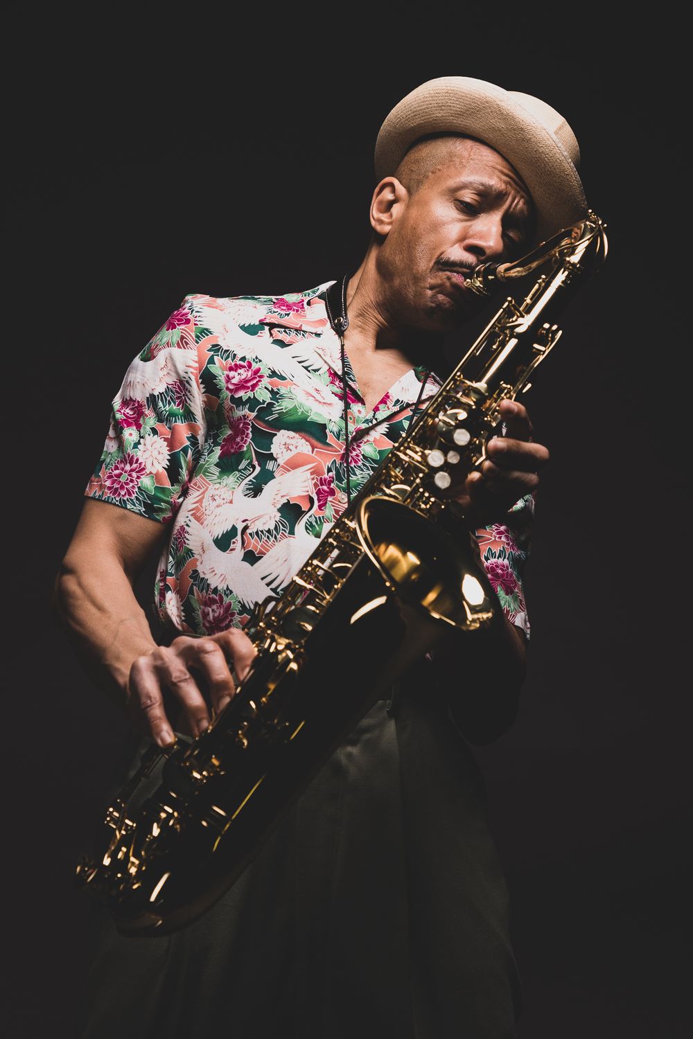 Jazz musician in floral shirt playing saxophone with passion against dark background.