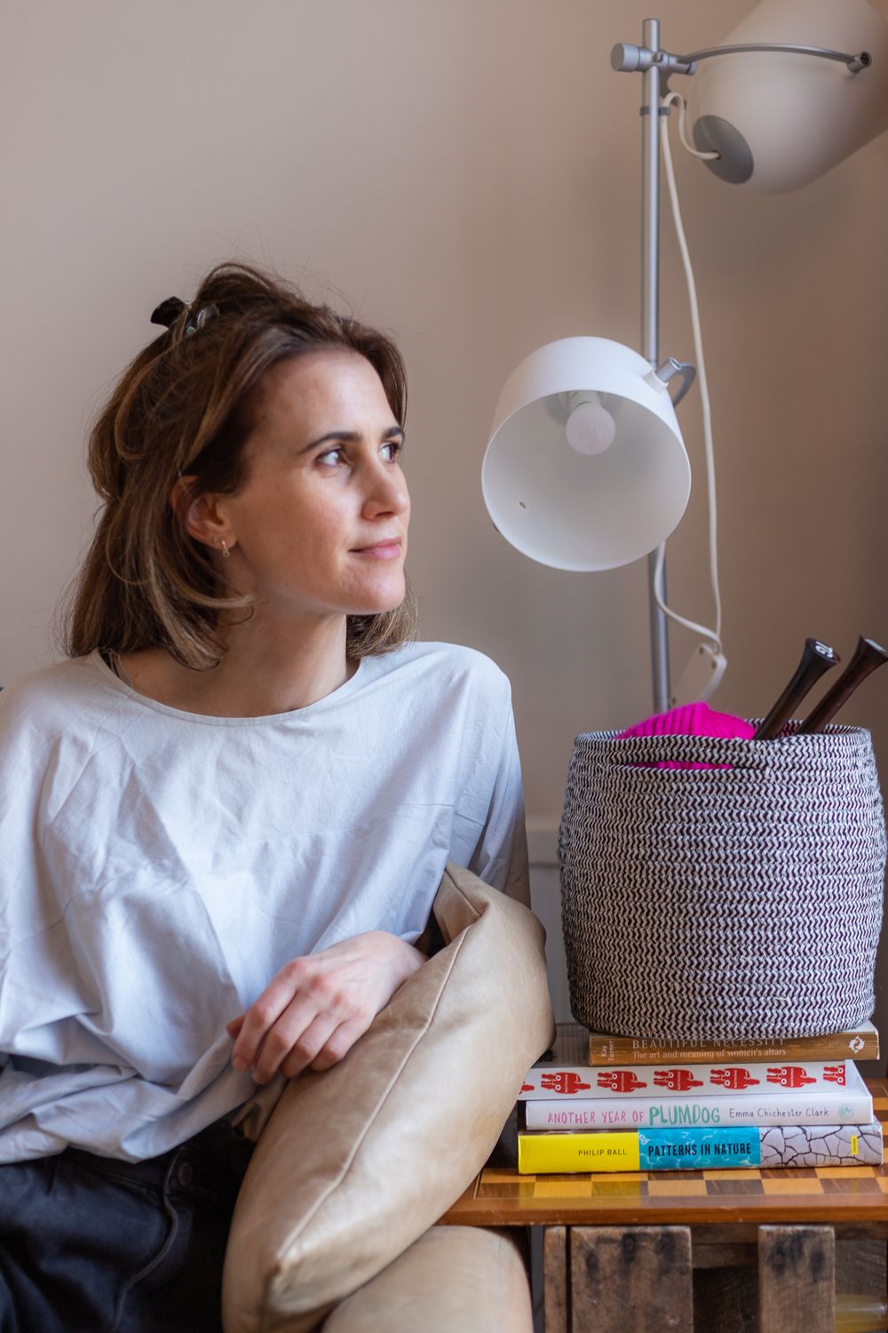 Woman relaxing by modern lamp with books and woven basket in cozy corner setting.