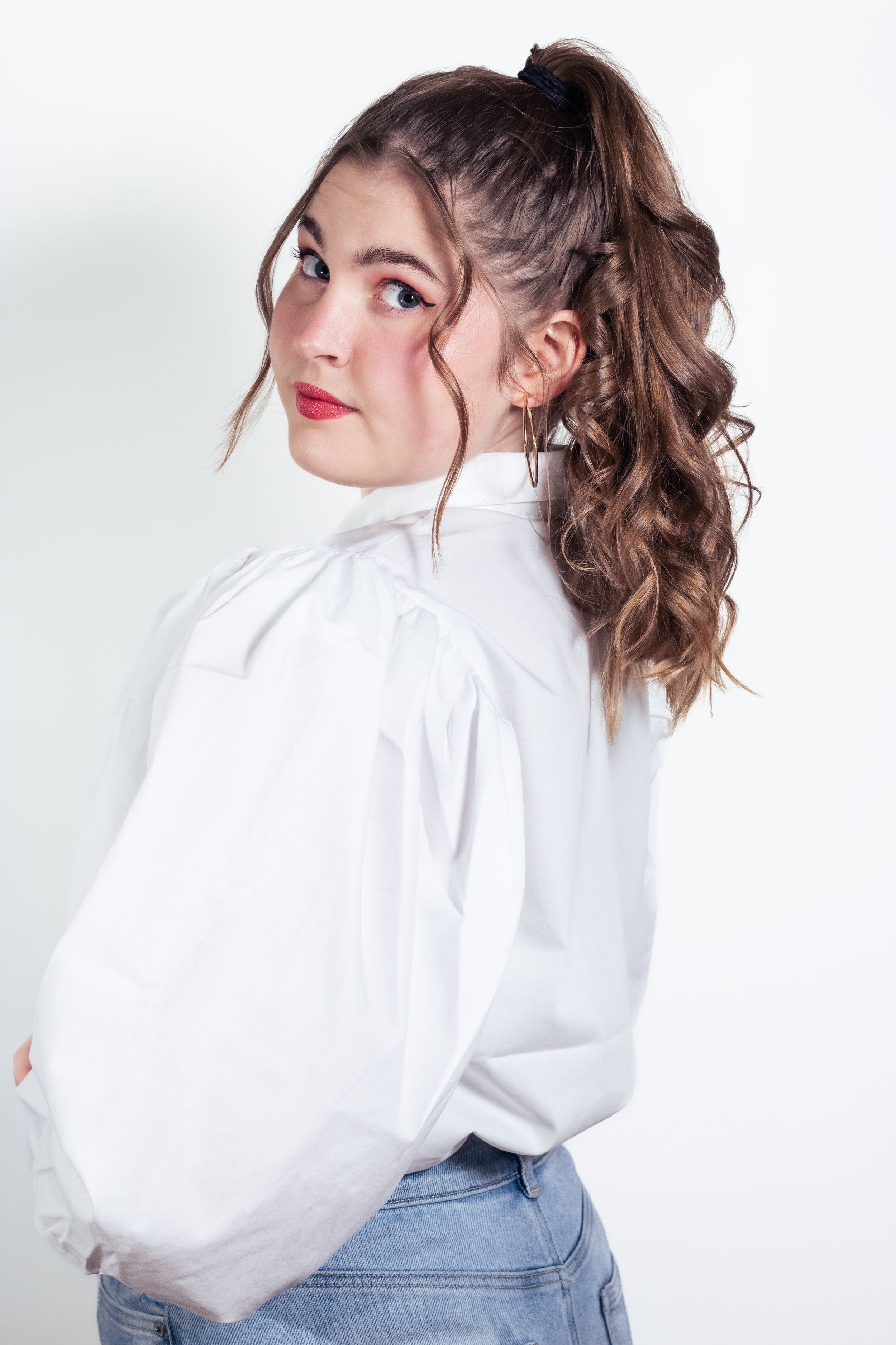 Fashion portrait of person in white blouse and jeans looking over shoulder.