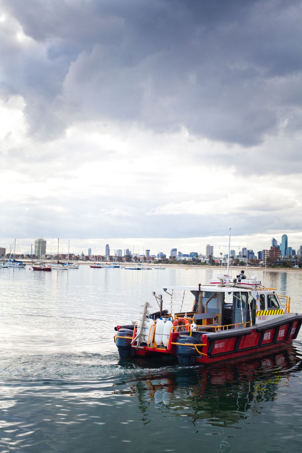 Red boat cruises through harbor with city skyline and dramatic clouds in background in Hong Kong.