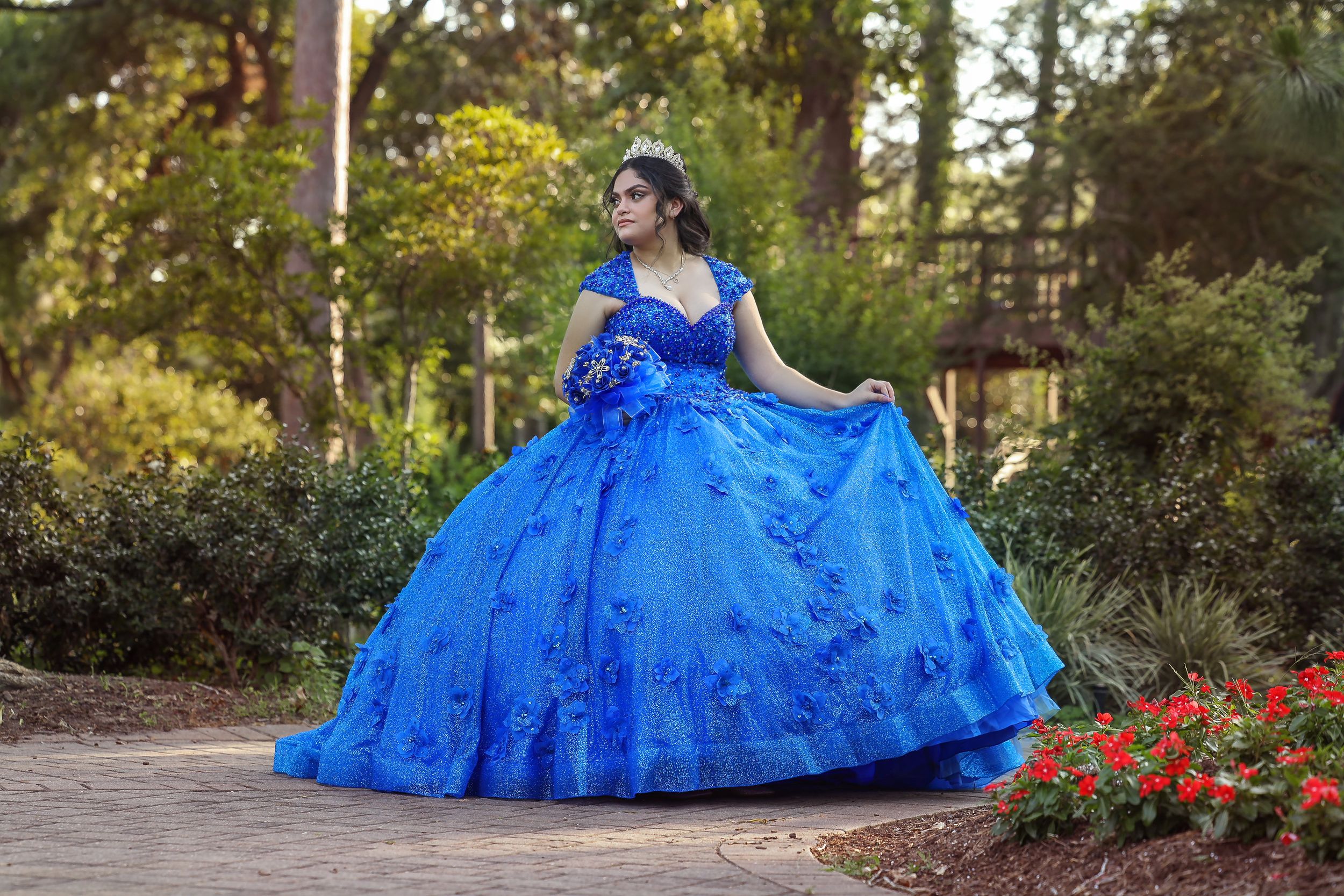 A royal blue ball gown with intricate details photographed in a garden setting.
