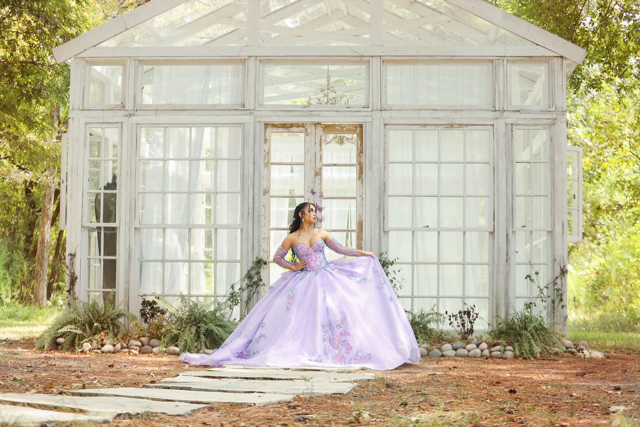 A lavender princess ball gown photographed in front of a glass greenhouse structure.
