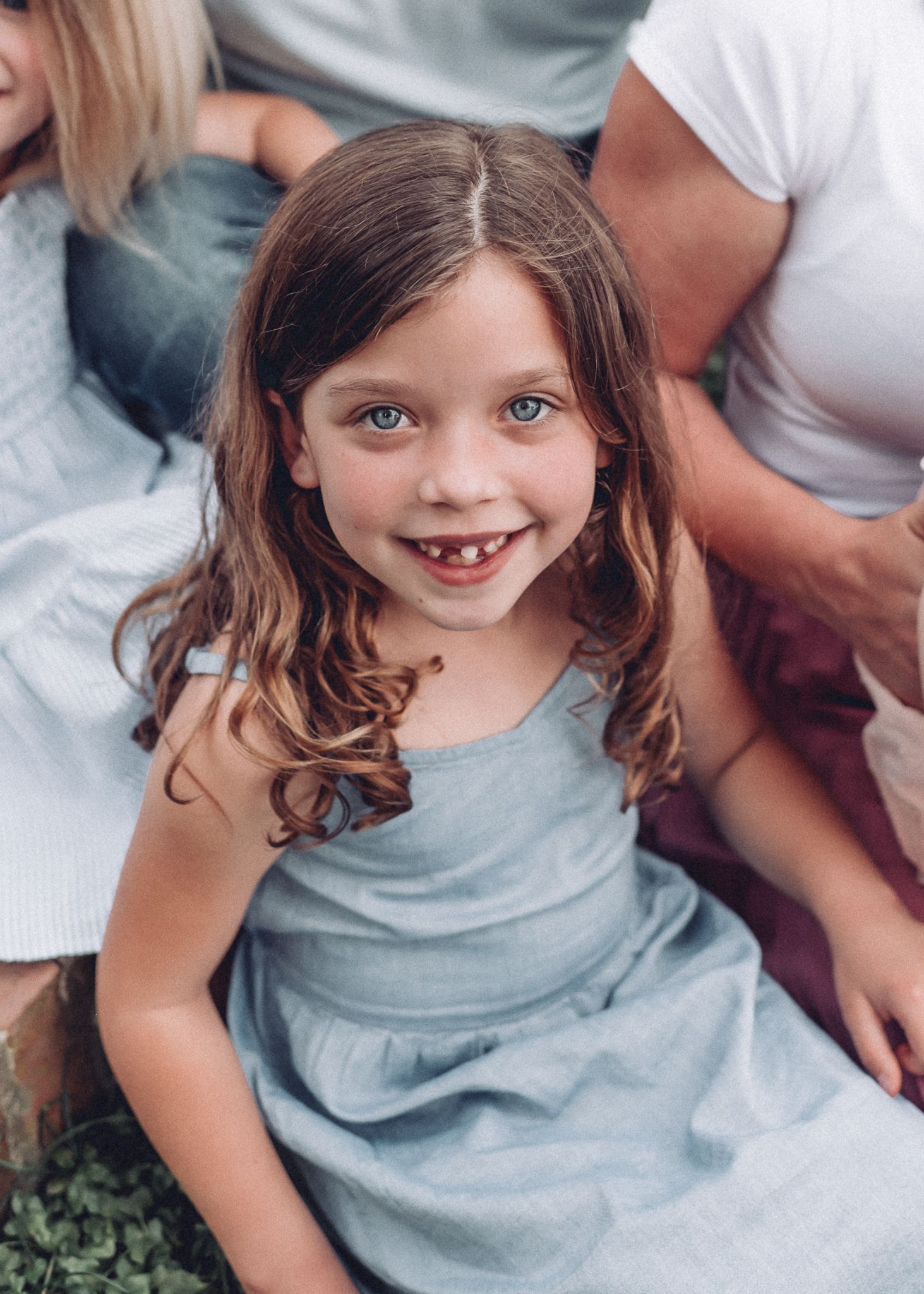A young child in a blue dress smiles at the camera during a casual photo session.
