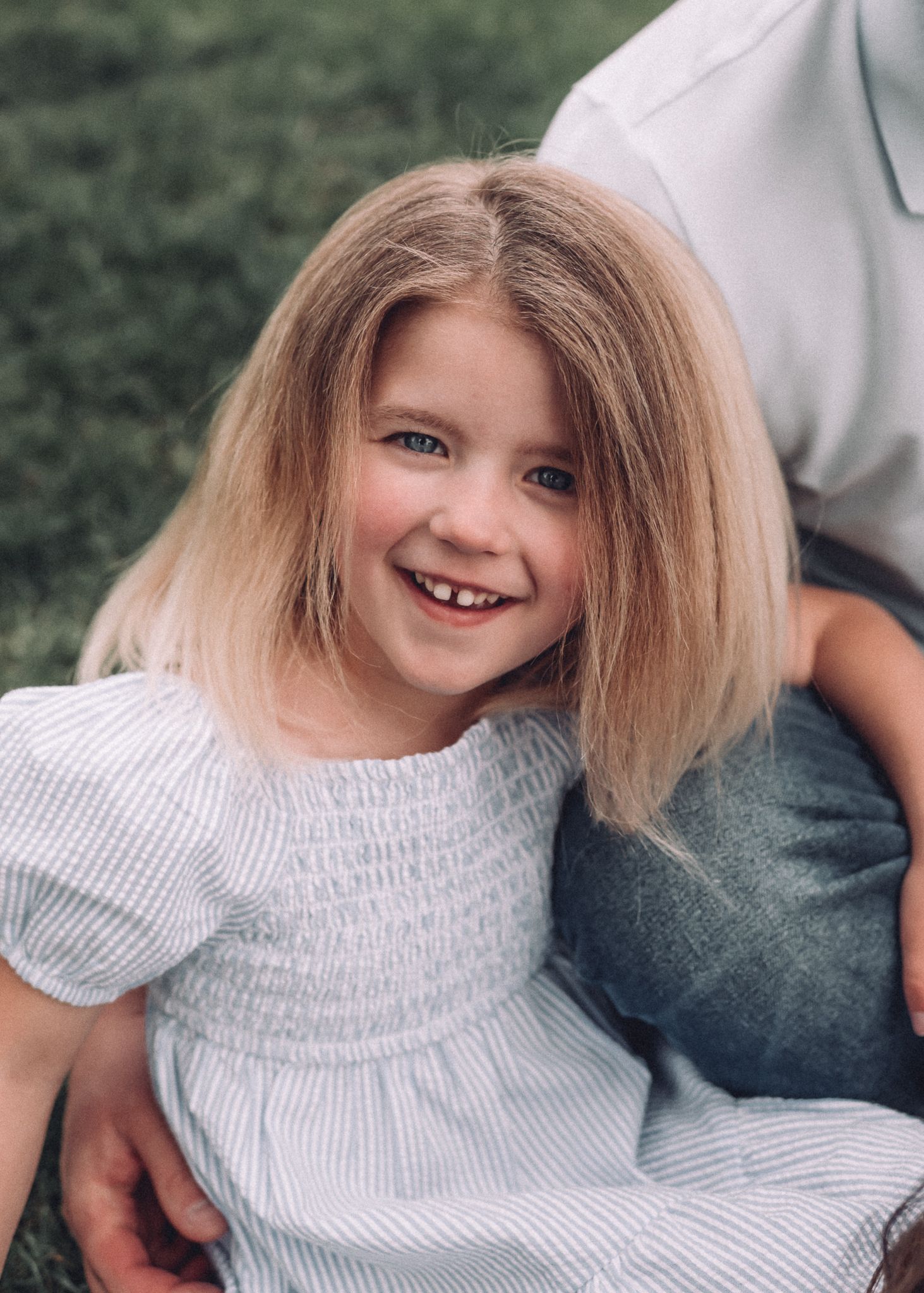 A child in a white smocked dress smiles brightly during an outdoor photo session.