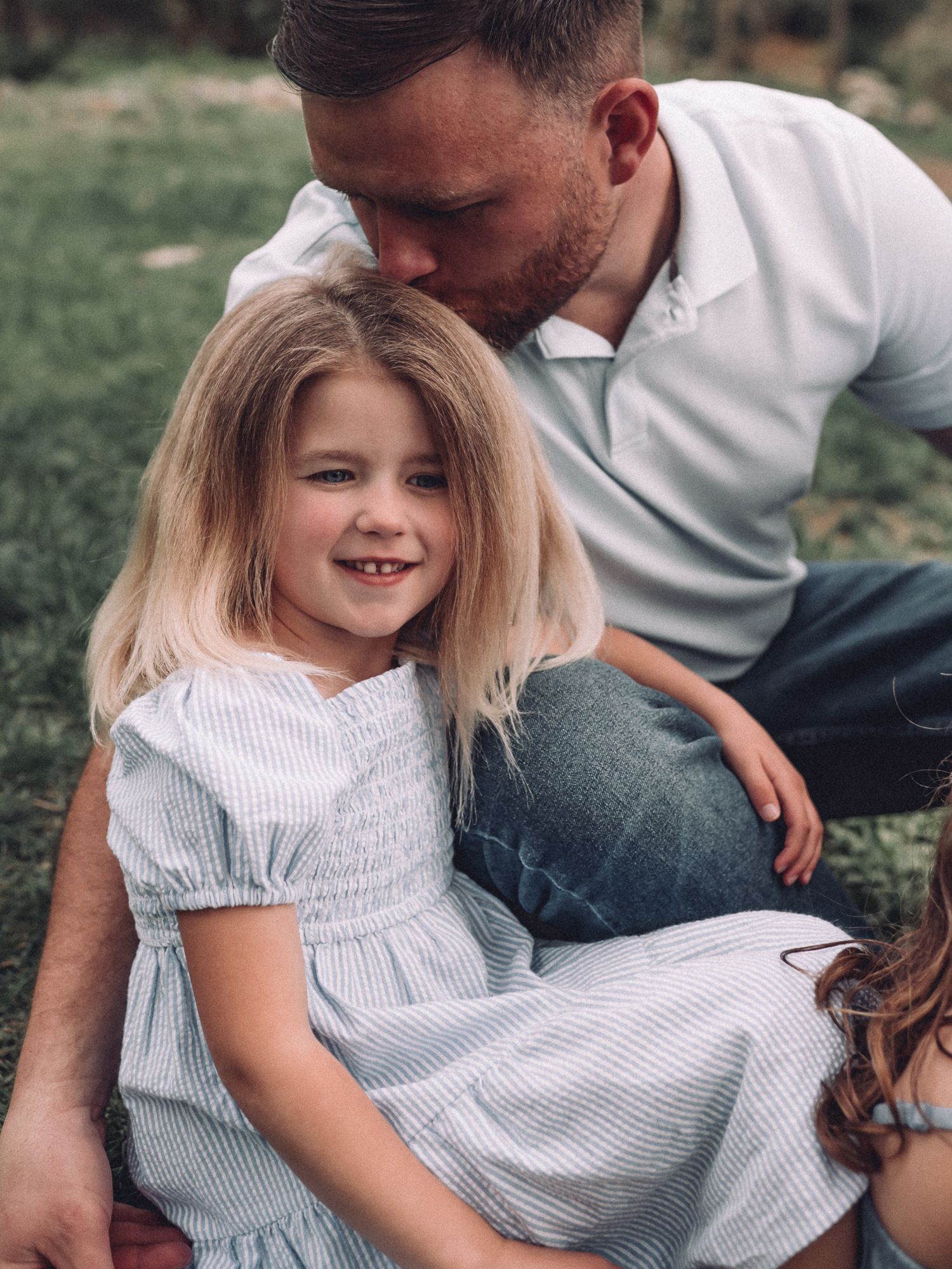 A tender family moment captured outdoors with natural lighting and greenery in background.