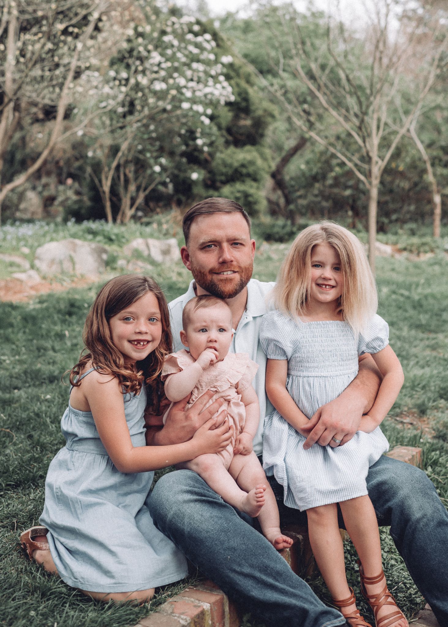 A spring family portrait outdoors with matching blue dresses and flowering trees in the background.