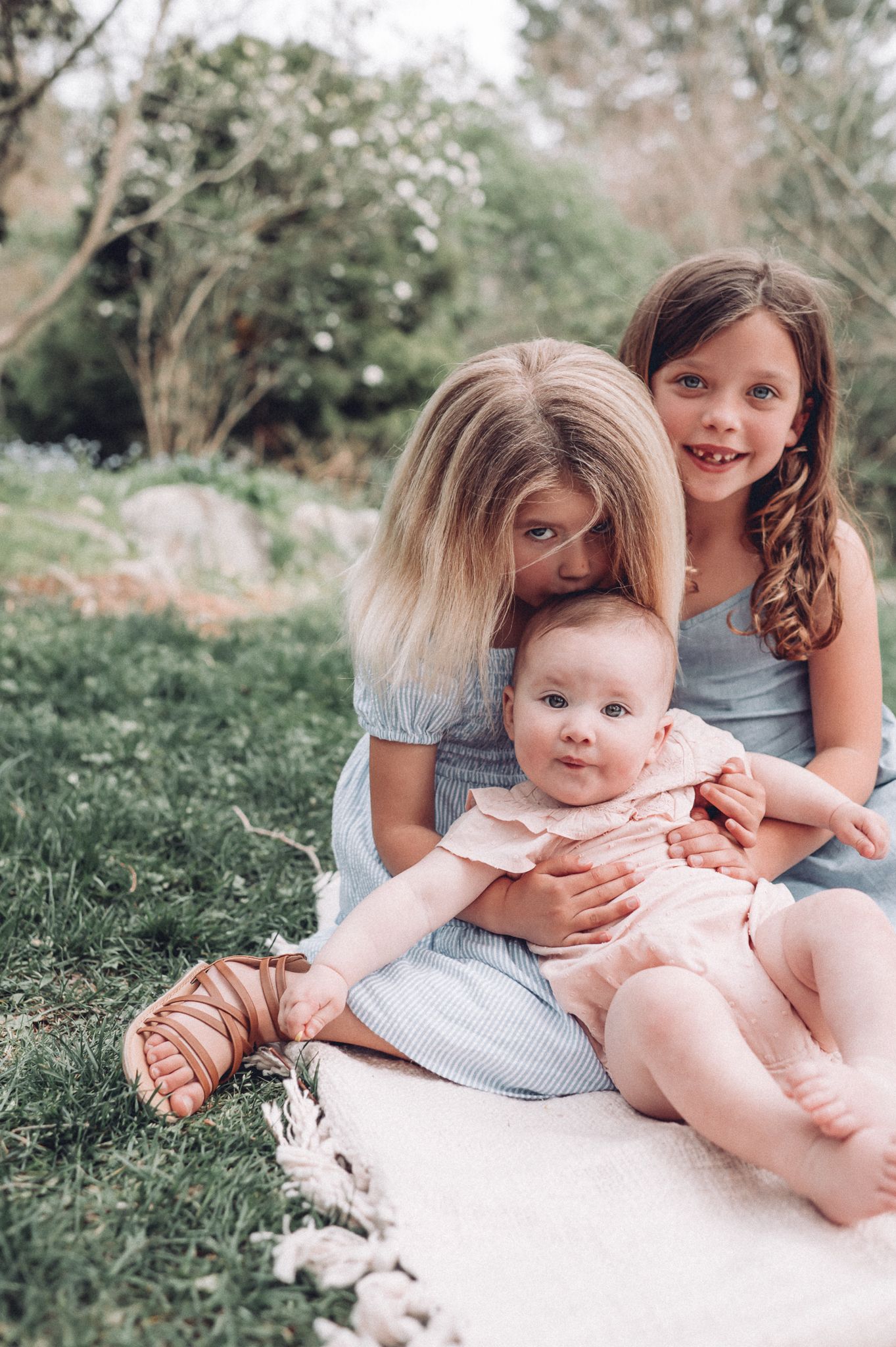 Siblings sharing sweet moments together on a white blanket in a garden setting.
