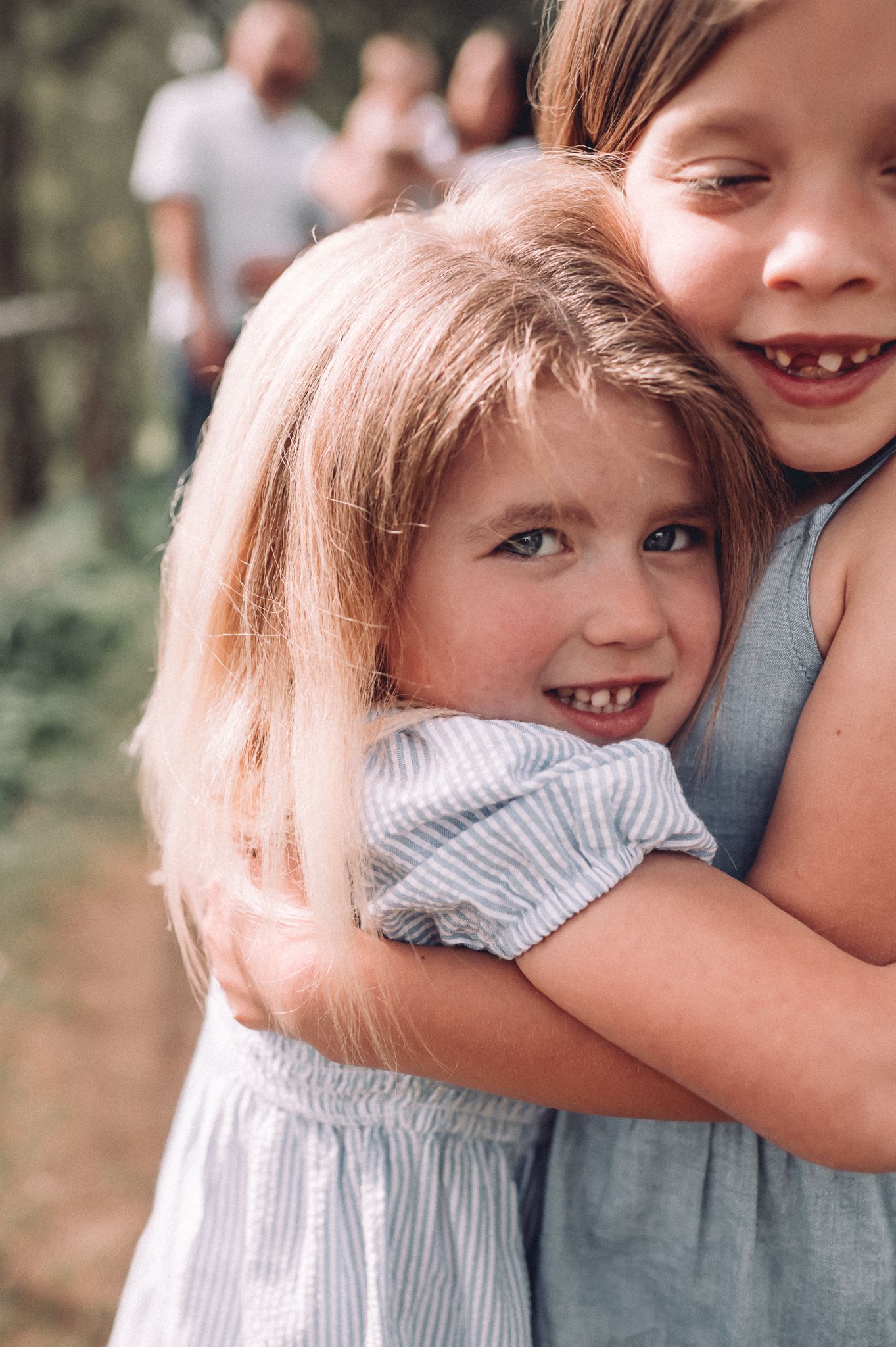 Two children share a joyful embrace outdoors while smiling and laughing together.