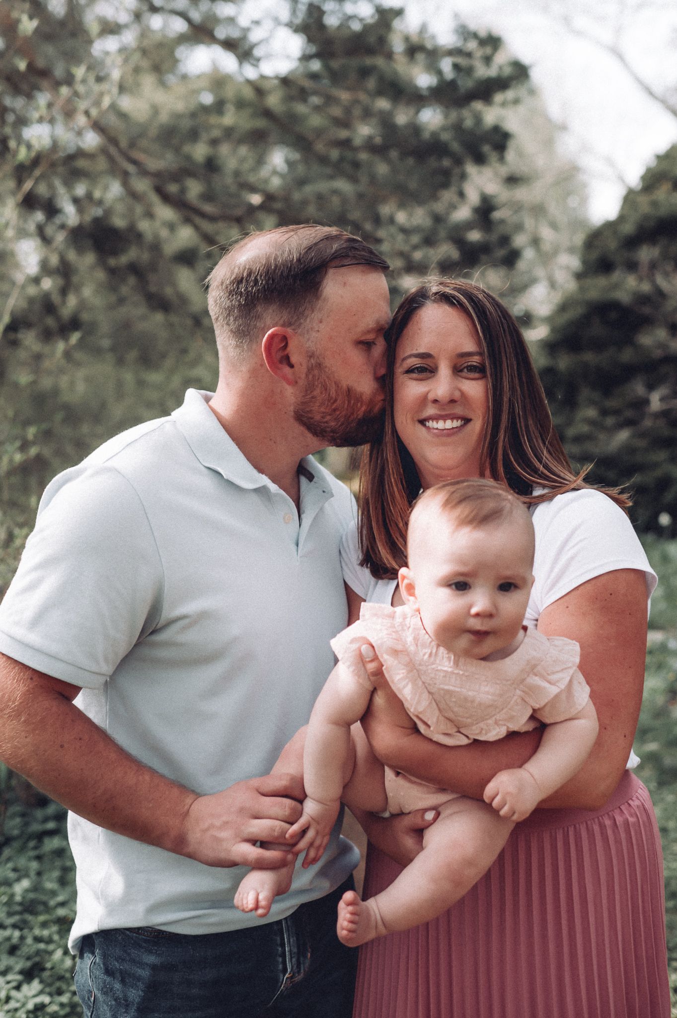 Family portrait in a garden setting with a small baby wearing a lace dress.