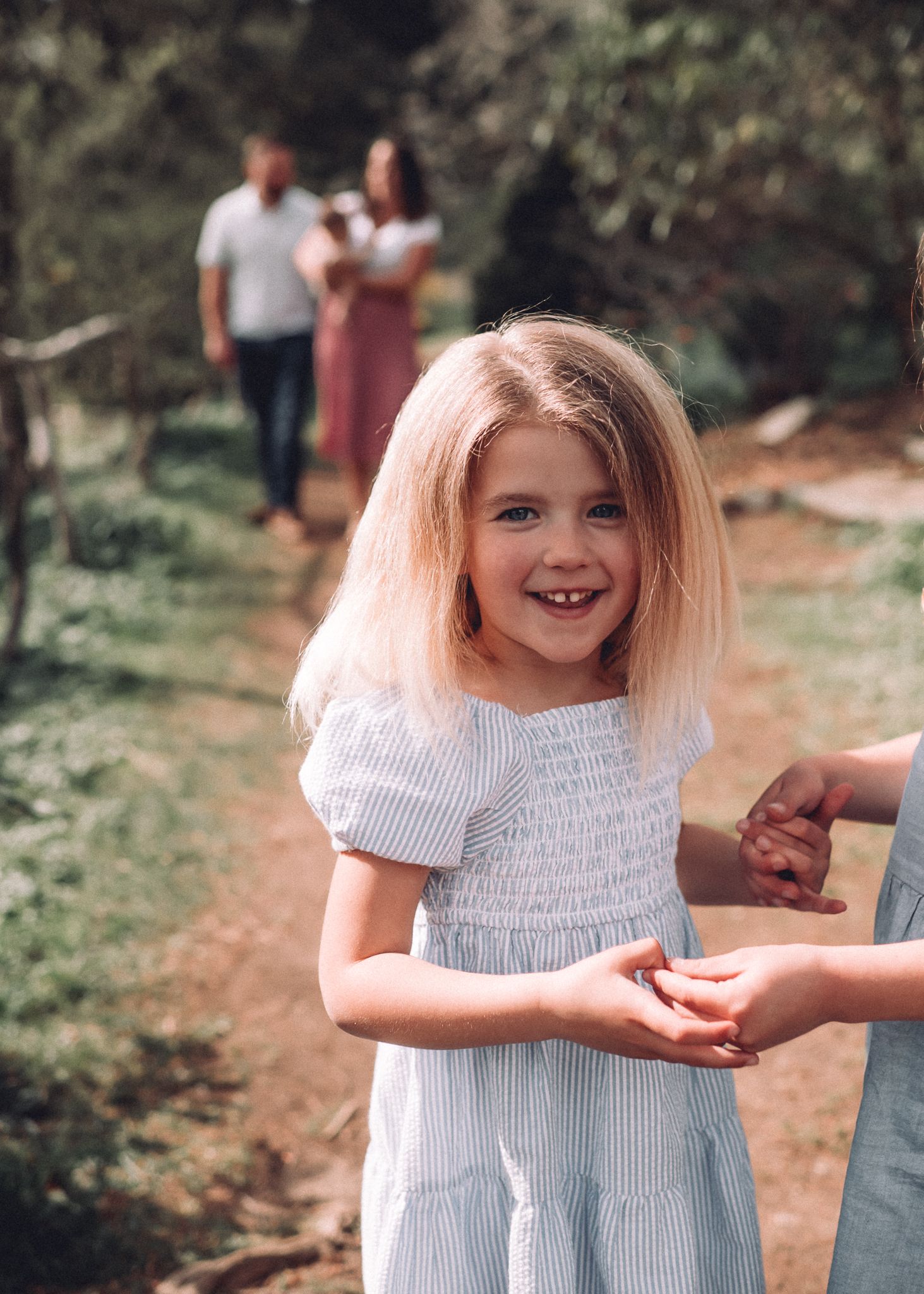 Young child in a blue and white striped dress smiles brightly during an outdoor photoshoot.