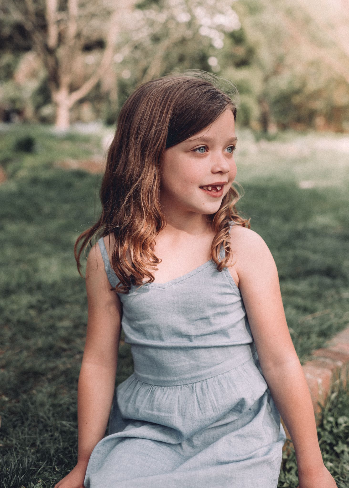 Child in a light blue dress poses outdoors during a sunny day.