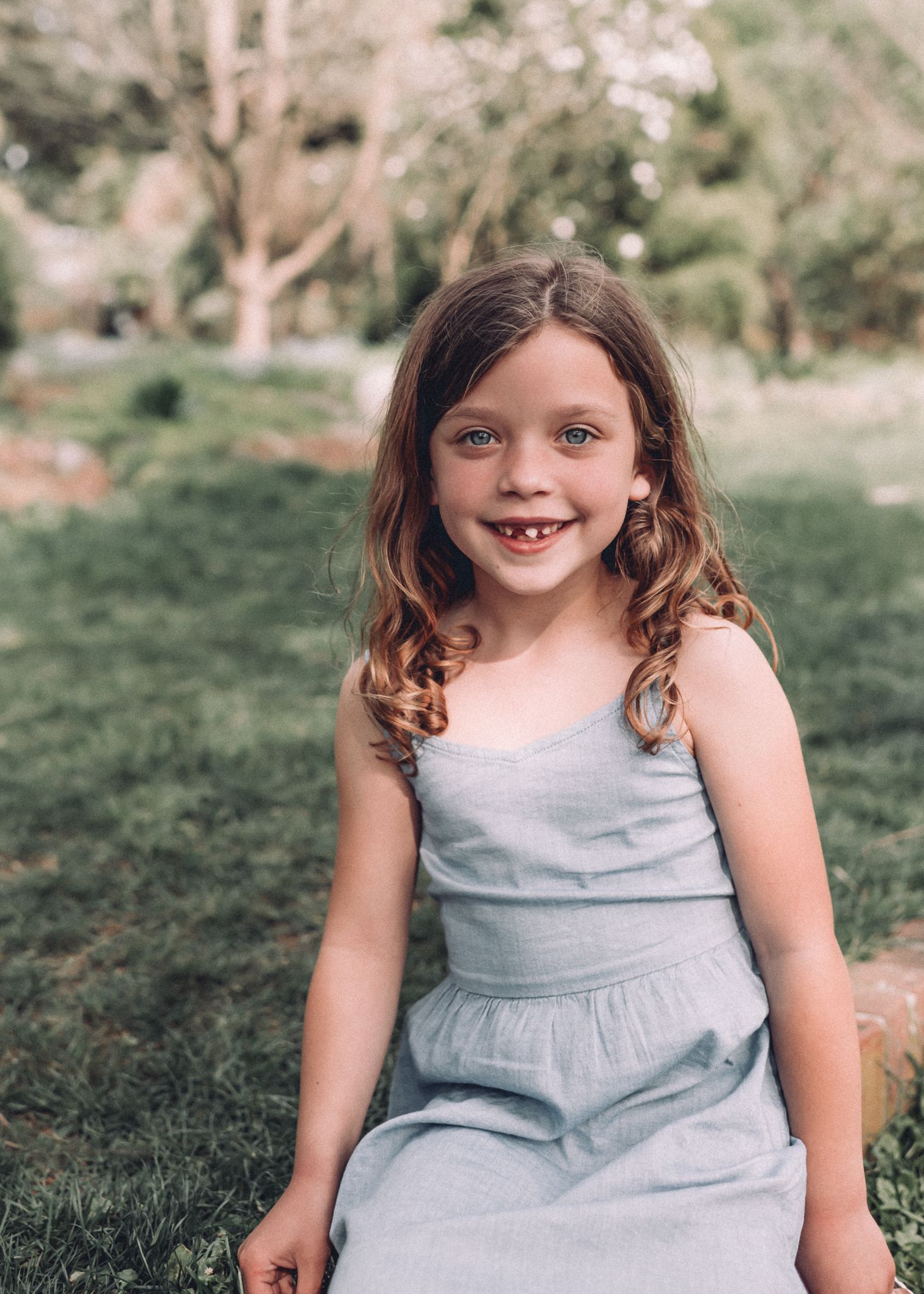 Child with curly hair in a blue dress smiles during an outdoor photo session.