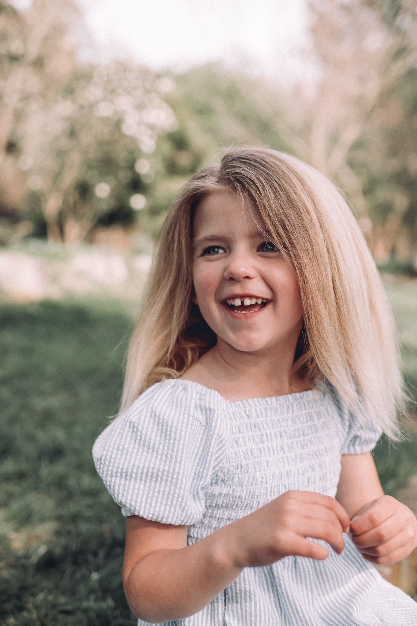 Child wearing a white smocked dress laughs joyfully during an outdoor photo session.