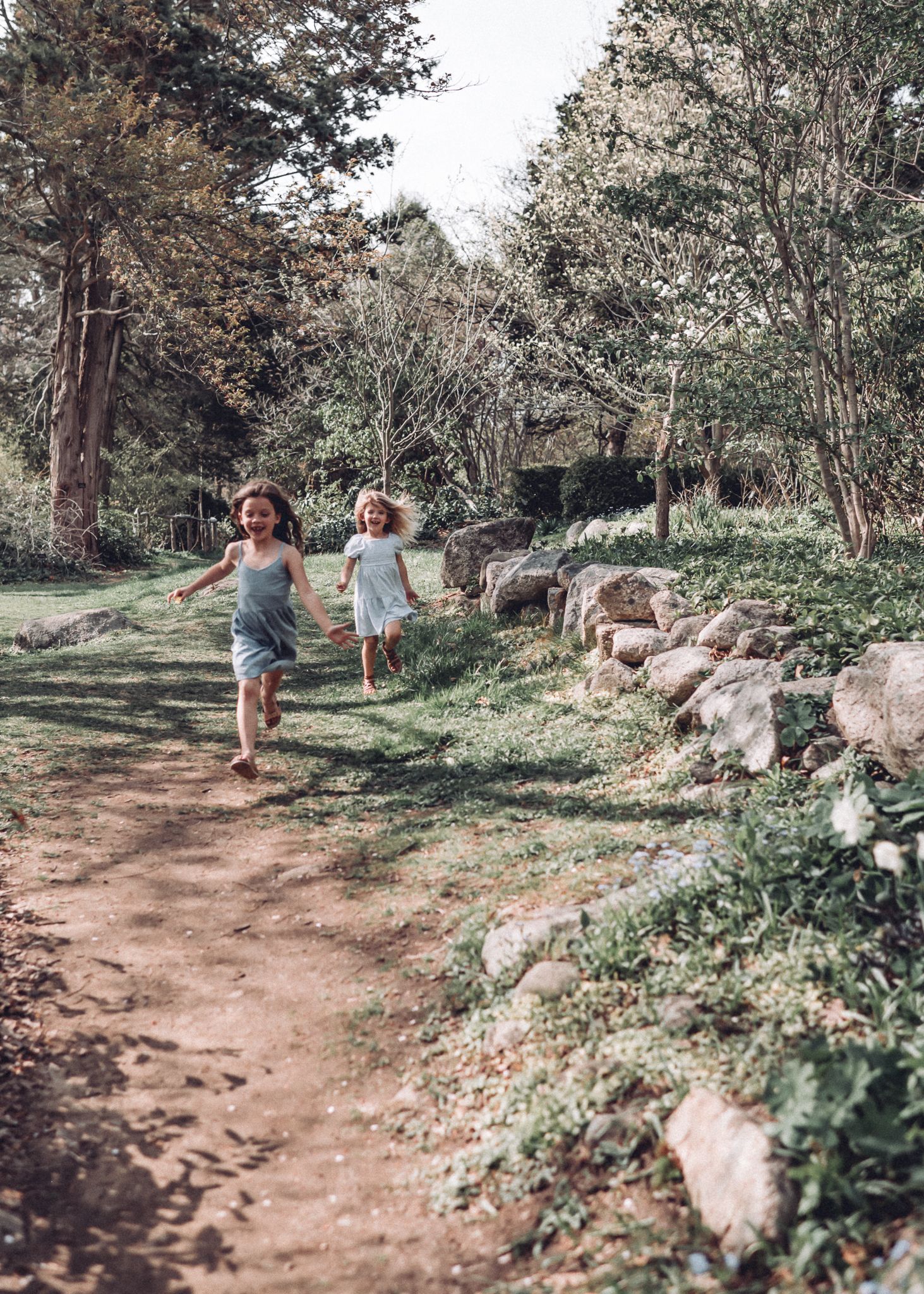 Two children run along a scenic wooded path lined with rocks.