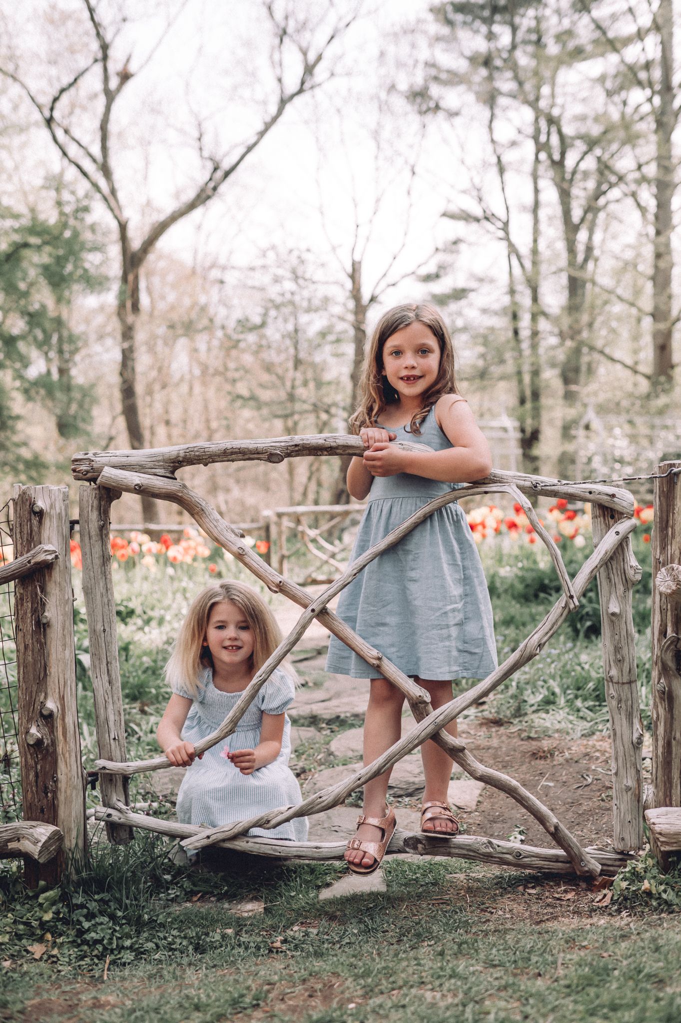 Children play and pose on rustic wooden garden gate surrounded by spring flowers.