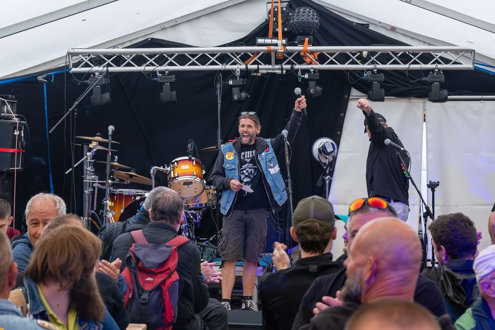 A lively outdoor music festival performance with a crowd gathered in front of a stage with lighting equipment.