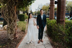 Couple walking together on sidewalk path surrounded by lush garden landscaping.