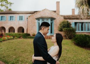 Romantic portrait in front of Spanish colonial mansion with palm trees and manicured lawn.
