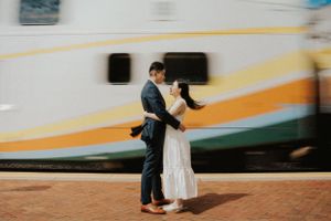 Romantic moment between couple embracing by passing train with orange and yellow stripes.