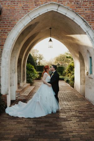 Dramatic wedding portrait under stone archway with flowing white gown and brick details.