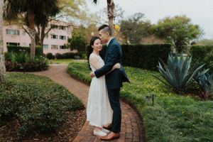 Romantic garden path portrait with couple embracing near tropical plants and curved walkway.