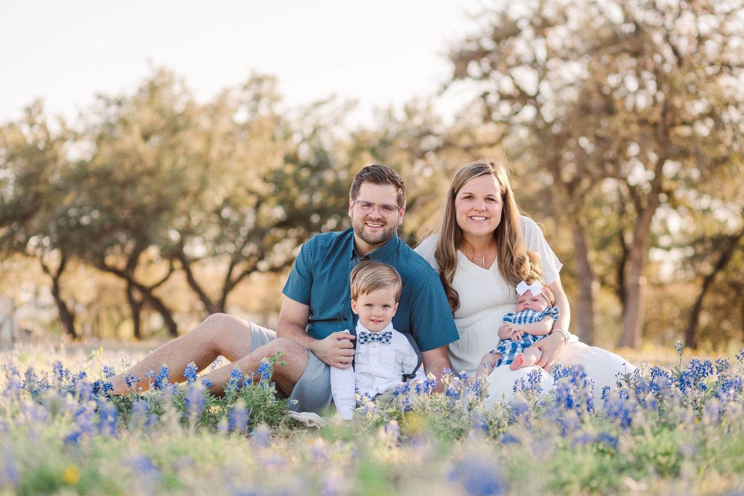 Family relaxing together in bluebonnet field during spring sunset photo session.