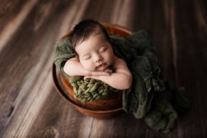 Artistic newborn portrait with dark moody lighting and green textured fabric.