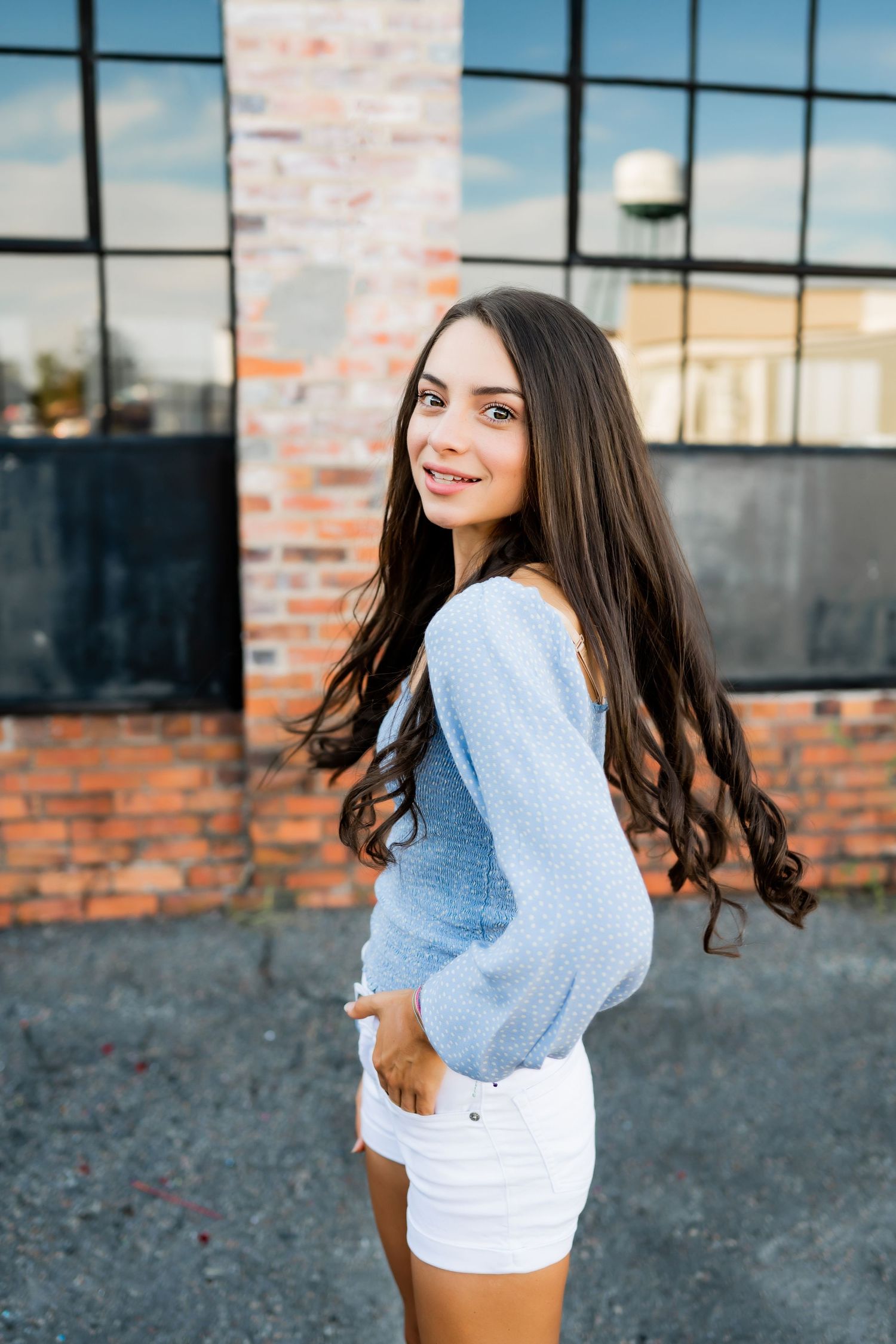 Urban fashion portrait against industrial backdrop wearing blue sweater and white shorts.